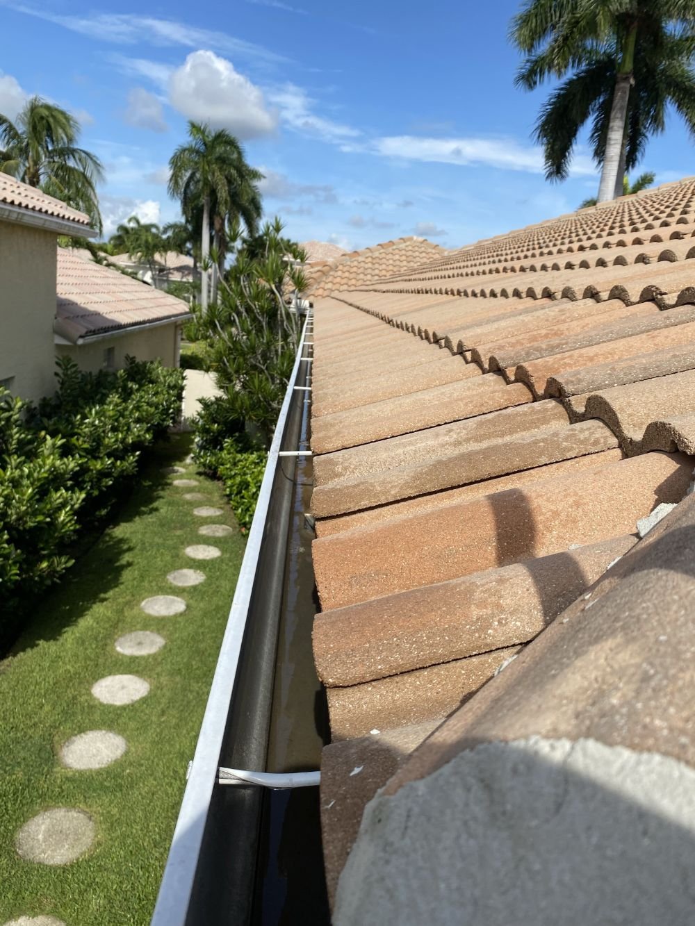 Aerial view of terracotta tile roofline with rain gutter, tropical palm trees, and manicured lawn with stepping stones below