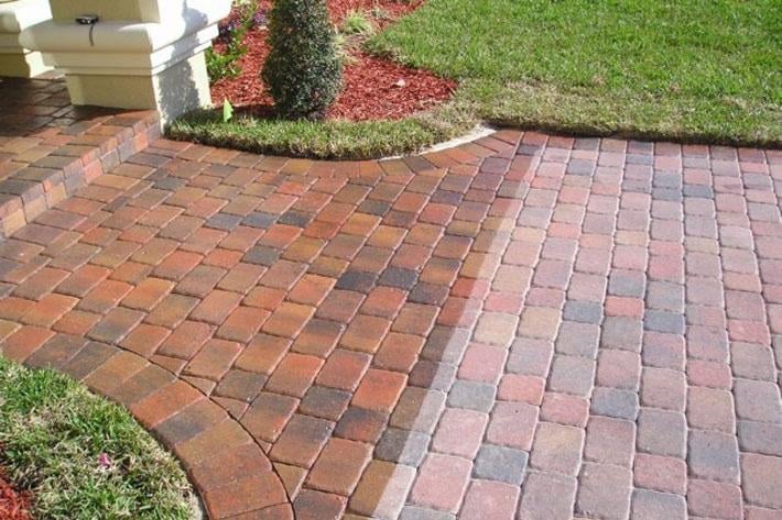 Curved brick patio with red and tan pavers, bordered by landscaping with green shrubs and red mulch